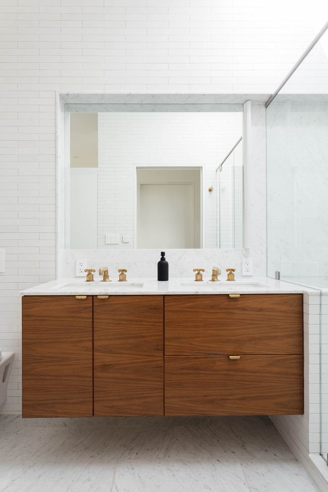 Photo of a medium sized contemporary ensuite bathroom in New York with flat-panel cabinets, dark wood cabinets, a corner shower, a wall mounted toilet, white tiles, ceramic tiles, white walls, marble flooring, a submerged sink, marble worktops, white floors, a hinged door and white worktops.