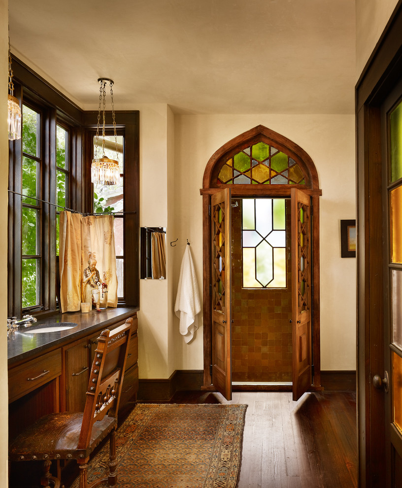 Imagen de cuarto de baño tradicional con lavabo bajoencimera, puertas de armario de madera oscura y ventanas