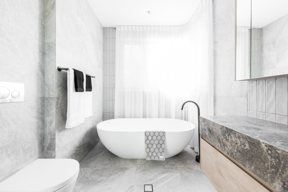 На фото: ванная комната в современном стиле с отдельно стоящей ванной и мраморной столешницей с