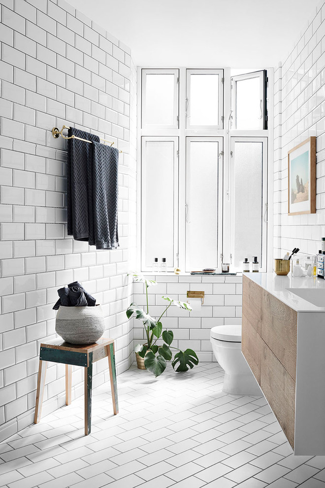 This is an example of a contemporary bathroom in New York with flat-panel cabinets, medium wood cabinets, white tiles, metro tiles, white walls, an integrated sink and white floors.