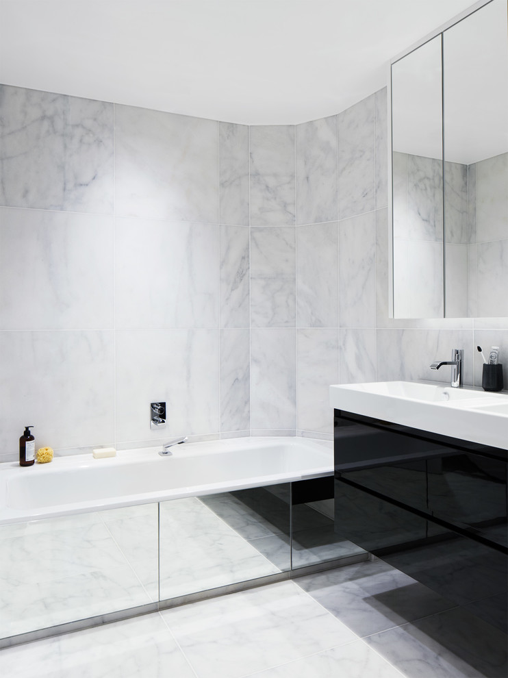 Inspiration for a large contemporary ensuite bathroom in London with a console sink, flat-panel cabinets, black cabinets, solid surface worktops, a built-in bath, an alcove shower, a wall mounted toilet, stone tiles, white walls, marble flooring and white tiles.