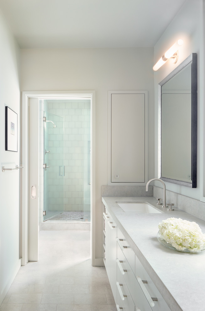 Cette photo montre une salle de bain principale moderne de taille moyenne avec un placard à porte plane, des portes de placard grises, une douche ouverte, un carrelage bleu, un carrelage en pâte de verre, un mur gris, un sol en calcaire, un lavabo encastré et un plan de toilette en calcaire.