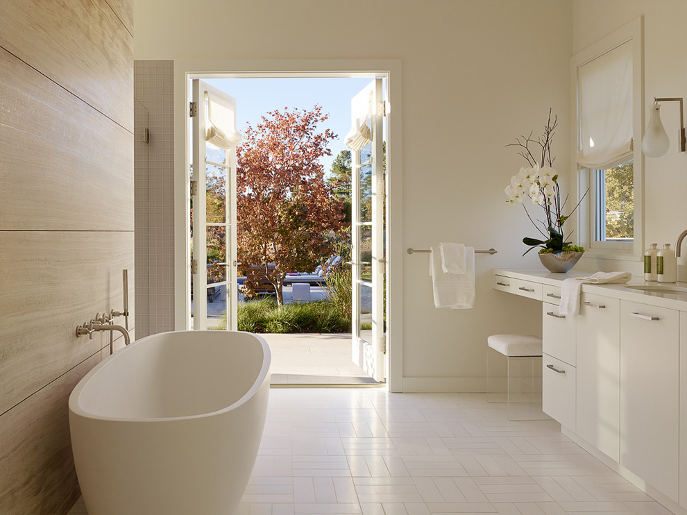 Cette image montre une grande salle de bain principale traditionnelle avec un lavabo encastré, un placard à porte plane, des portes de placard blanches, une baignoire indépendante et un mur blanc.