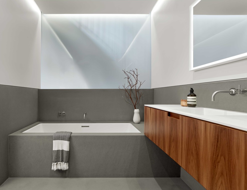Photo of a medium sized contemporary ensuite bathroom in San Francisco with freestanding cabinets, medium wood cabinets, a built-in bath, a built-in shower, a wall mounted toilet, stone slabs, grey walls, limestone flooring, an integrated sink, solid surface worktops, grey floors and a sliding door.