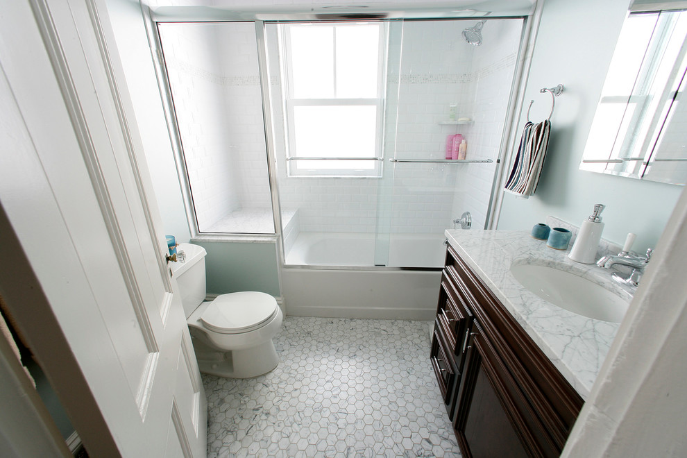 Inredning av ett klassiskt litet badrum, med skåp i mörkt trä, ett badkar i en alkov, en dusch/badkar-kombination, en toalettstol med separat cisternkåpa, vit kakel, keramikplattor, blå väggar, marmorgolv, ett undermonterad handfat och marmorbänkskiva