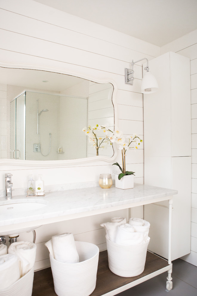 Inredning av ett klassiskt badrum med dusch, med vita skåp, en hörndusch, vita väggar, marmorbänkskiva, öppna hyllor, vit kakel, mosaik och ett undermonterad handfat