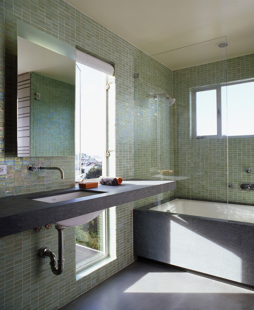Idee per una stanza da bagno padronale moderna di medie dimensioni con vasca/doccia, piastrelle verdi, piastrelle di vetro, pareti verdi, pavimento in cemento, lavabo sottopiano, top in pietra calcarea e vasca sottopiano