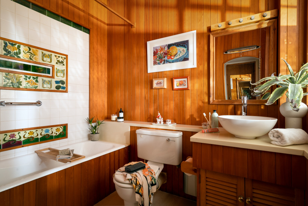 Aménagement d'une salle de bain bord de mer en bois brun et bois avec un placard à porte persienne, une baignoire encastrée, un combiné douche/baignoire, WC séparés, un carrelage multicolore, un mur marron, une vasque, une cabine de douche avec un rideau, un plan de toilette beige, meuble simple vasque et meuble-lavabo encastré.