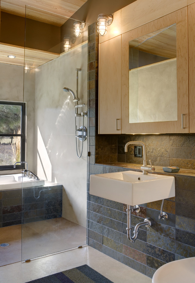 На фото: главная ванная комната в современном стиле с плоскими фасадами, светлыми деревянными фасадами, ванной в нише, разноцветной плиткой, каменной плиткой, серыми стенами, бетонным полом, подвесной раковиной и открытым душем с