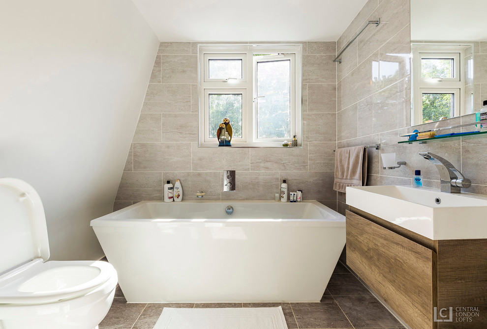 Contemporary ensuite bathroom in London with glass-front cabinets, a freestanding bath, a one-piece toilet, brown tiles, beige walls, ceramic flooring and a wall-mounted sink.