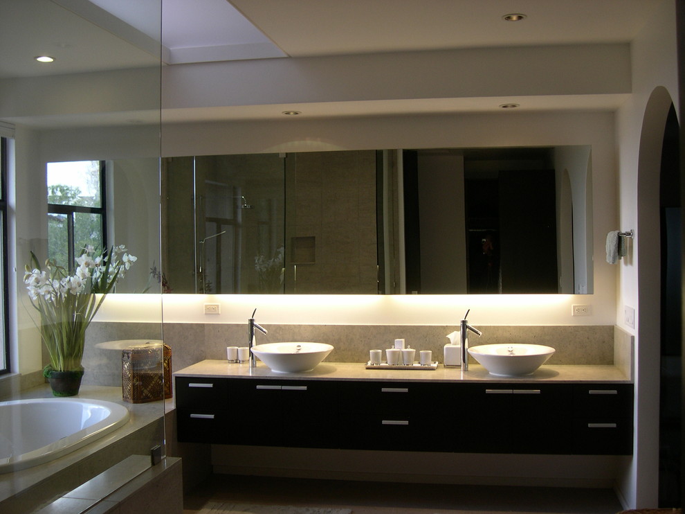 Идея дизайна: большая главная ванная комната в стиле модернизм с настольной раковиной, плоскими фасадами, темными деревянными фасадами, столешницей из известняка, гидромассажной ванной, открытым душем, унитазом-моноблоком, серой плиткой, каменной плиткой, белыми стенами и полом из известняка