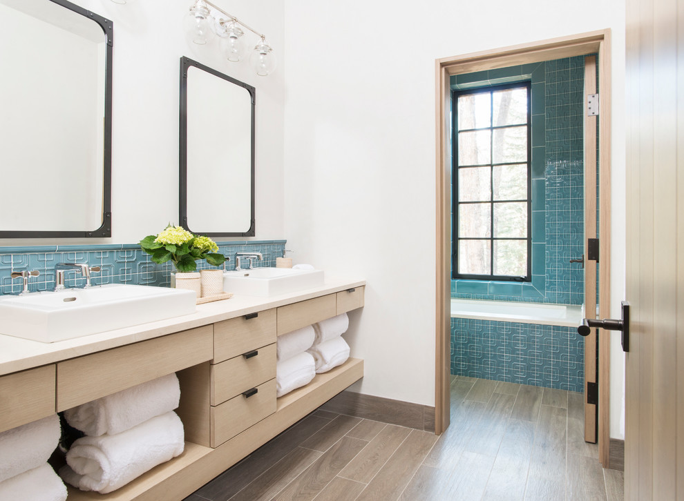 Ispirazione per una stanza da bagno stile rurale con ante lisce, ante in legno chiaro, vasca sottopiano, piastrelle blu, pareti bianche, lavabo a bacinella e pavimento marrone