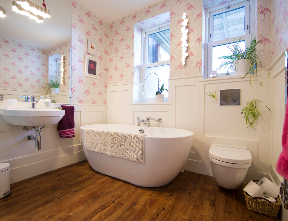 Foto di una stanza da bagno eclettica di medie dimensioni con vasca freestanding, WC sospeso, pavimento in legno massello medio, lavabo sospeso e pavimento marrone