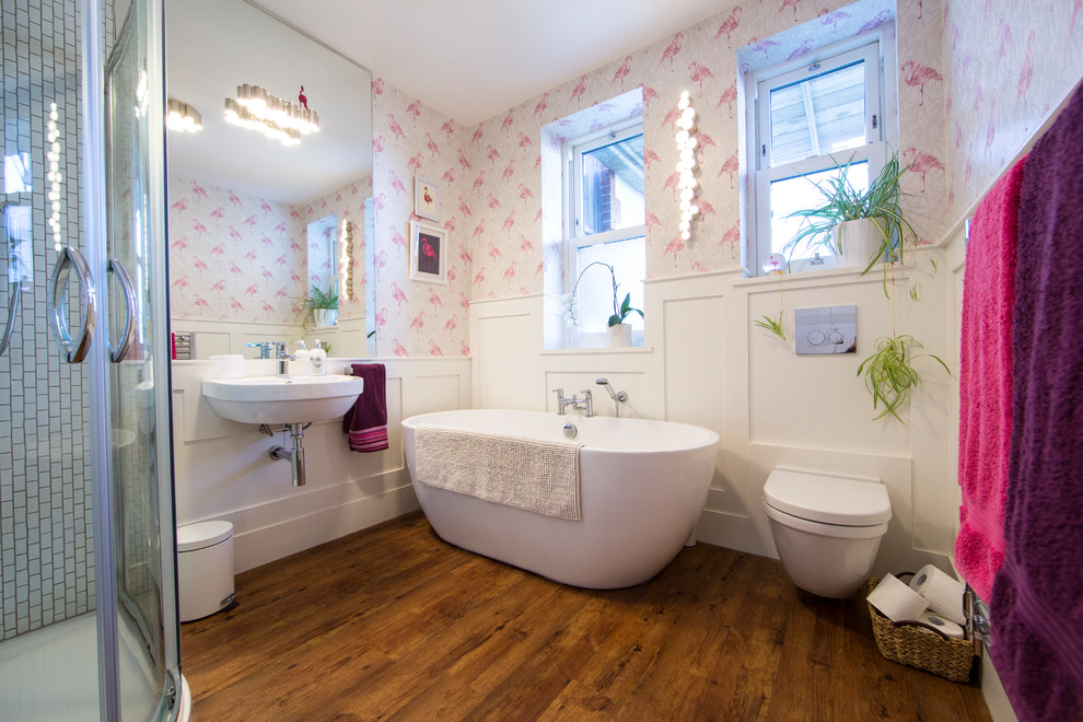 Immagine di una stanza da bagno per bambini minimalista di medie dimensioni con vasca freestanding, doccia ad angolo, WC sospeso, piastrelle bianche, piastrelle a mosaico, pareti bianche, pavimento in laminato, lavabo sospeso, pavimento marrone e porta doccia scorrevole