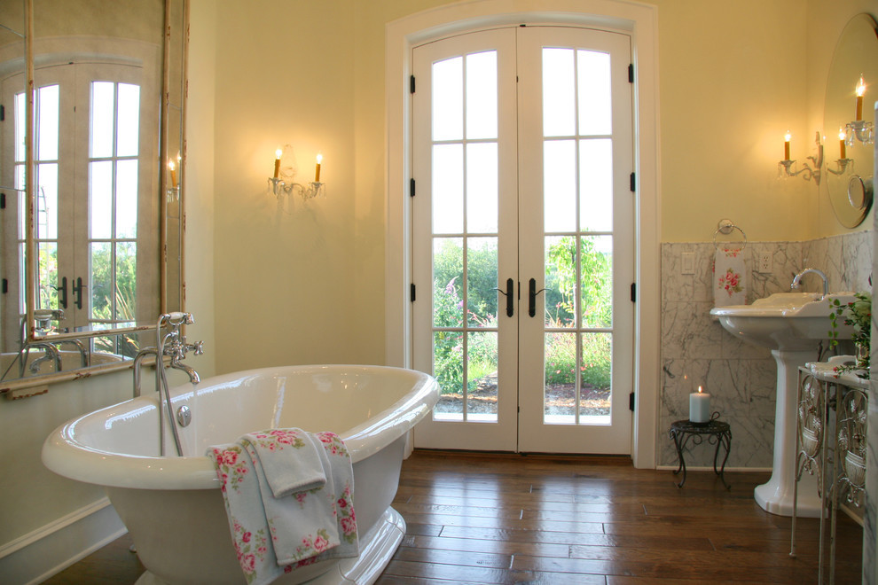 Cette photo montre une salle de bain principale victorienne avec un lavabo de ferme, une baignoire indépendante, un carrelage gris, un mur jaune et un sol en bois brun.