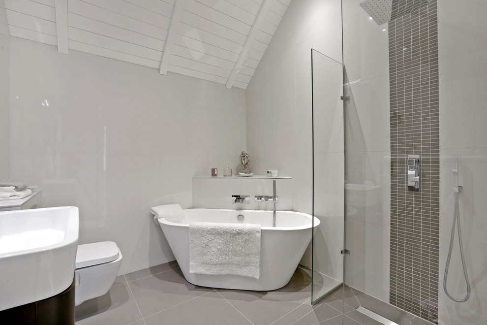 This is an example of a contemporary ensuite bathroom in Hertfordshire with a freestanding bath, a corner shower, grey tiles, grey walls, an integrated sink, grey floors and a hinged door.