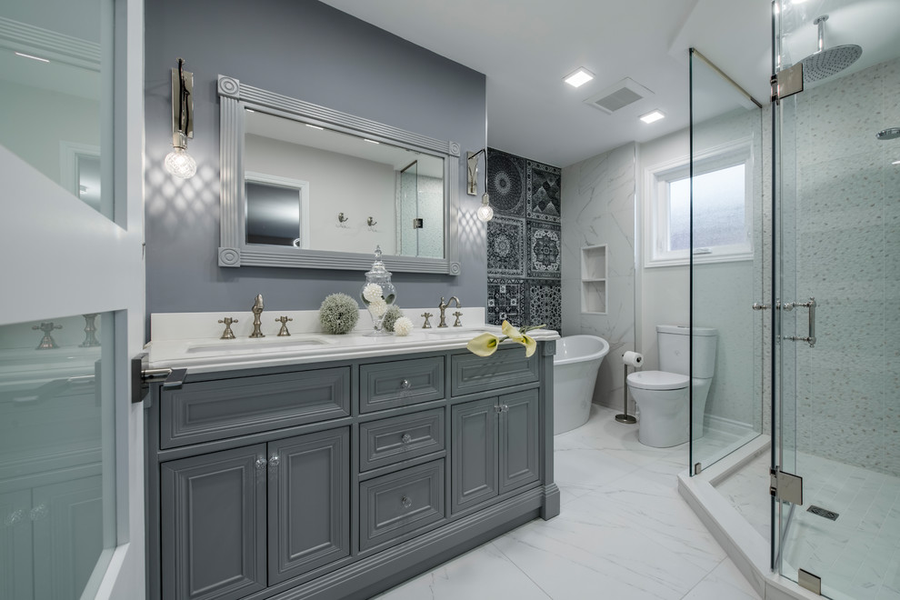 Inspiration for a medium sized traditional ensuite bathroom in Toronto with recessed-panel cabinets, grey cabinets, a freestanding bath, a corner shower, a two-piece toilet, black and white tiles, ceramic tiles, white walls, marble flooring, a submerged sink, quartz worktops, white floors, a hinged door and white worktops.