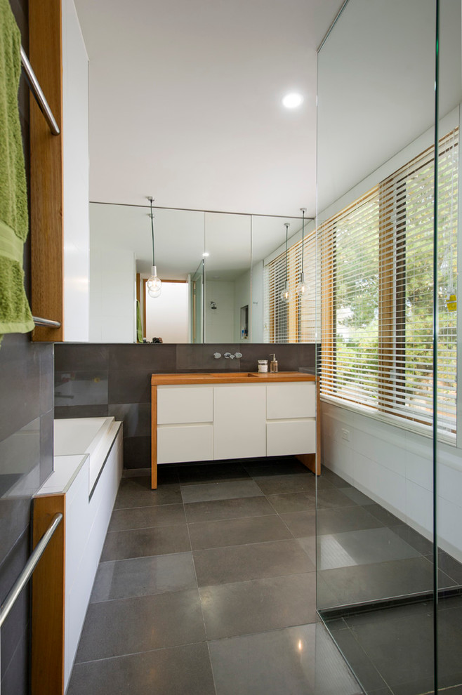 Modern inredning av ett mellanstort brun brunt badrum med dusch, med släta luckor, vita skåp, ett platsbyggt badkar, en öppen dusch, vit kakel, vita väggar, betonggolv, ett integrerad handfat, träbänkskiva, grått golv och med dusch som är öppen