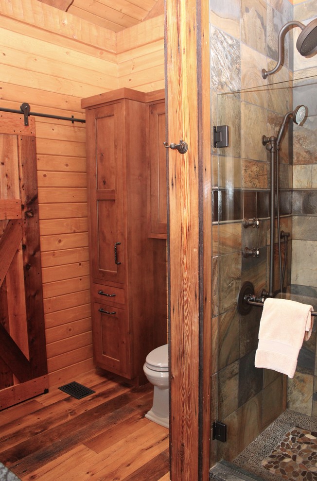 Photo of a medium sized rustic shower room bathroom in Other with shaker cabinets, medium wood cabinets, an alcove shower, a two-piece toilet, stone tiles, brown walls, medium hardwood flooring, a built-in sink and granite worktops.