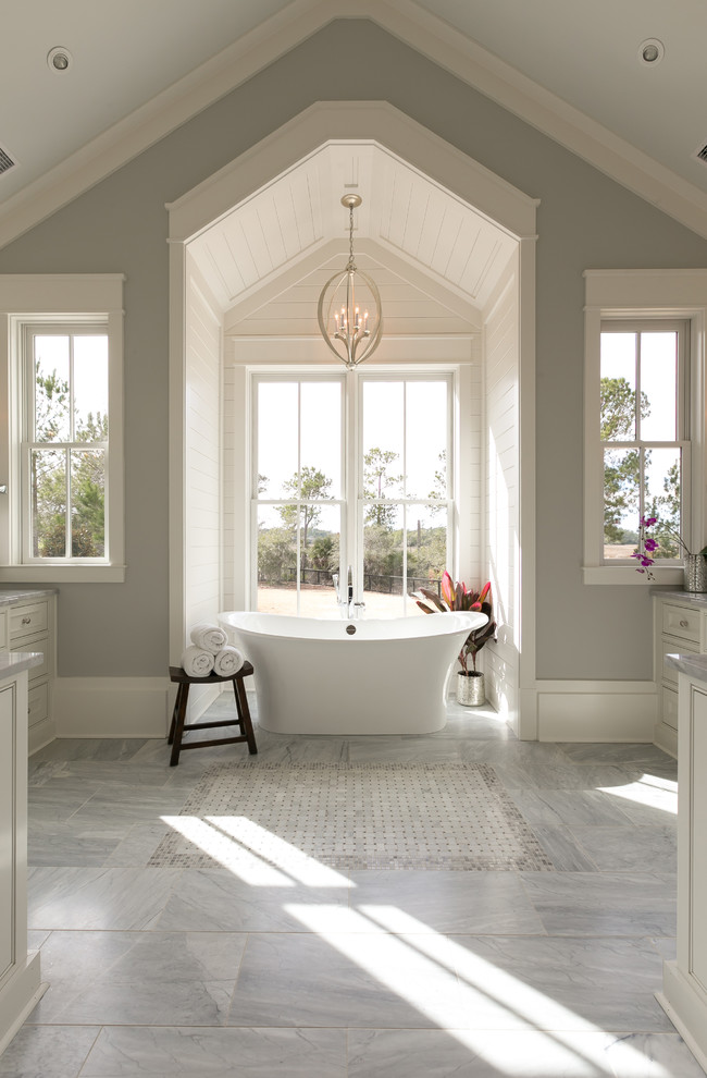 Réalisation d'une salle de bain principale et grise et blanche marine avec une baignoire indépendante, un mur gris et une fenêtre.