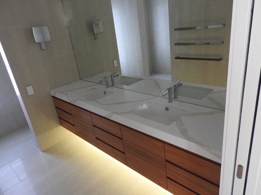Example of a trendy beige tile and travertine tile travertine floor and beige floor bathroom design in Gold Coast - Tweed with flat-panel cabinets, medium tone wood cabinets, a one-piece toilet, an undermount sink and marble countertops