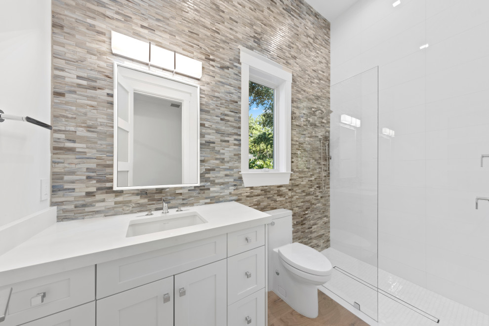 Example of a mid-sized transitional 3/4 beige tile, brown tile, gray tile and matchstick tile light wood floor and beige floor bathroom design in Miami with recessed-panel cabinets, white cabinets, a one-piece toilet, white walls, an undermount sink, quartz countertops and white countertops
