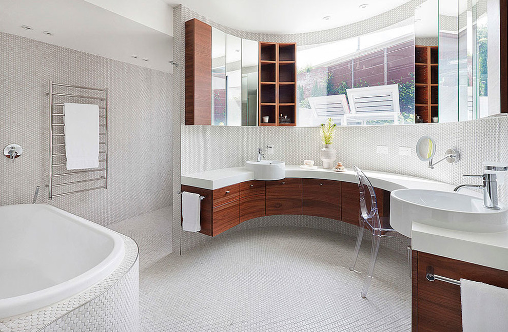 На фото: большая главная ванная комната в современном стиле с плоскими фасадами, светлыми деревянными фасадами, белой плиткой, плиткой мозаикой, белыми стенами, полом из мозаичной плитки, настольной раковиной, столешницей из искусственного камня, накладной ванной и белым полом с