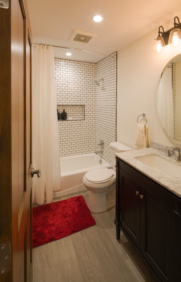 Cette photo montre une salle d'eau chic de taille moyenne avec un placard à porte shaker, des portes de placard noires, une baignoire en alcôve, un combiné douche/baignoire, WC séparés, un carrelage blanc, un carrelage métro, un mur beige, un sol en carrelage de porcelaine, un lavabo encastré et un plan de toilette en marbre.