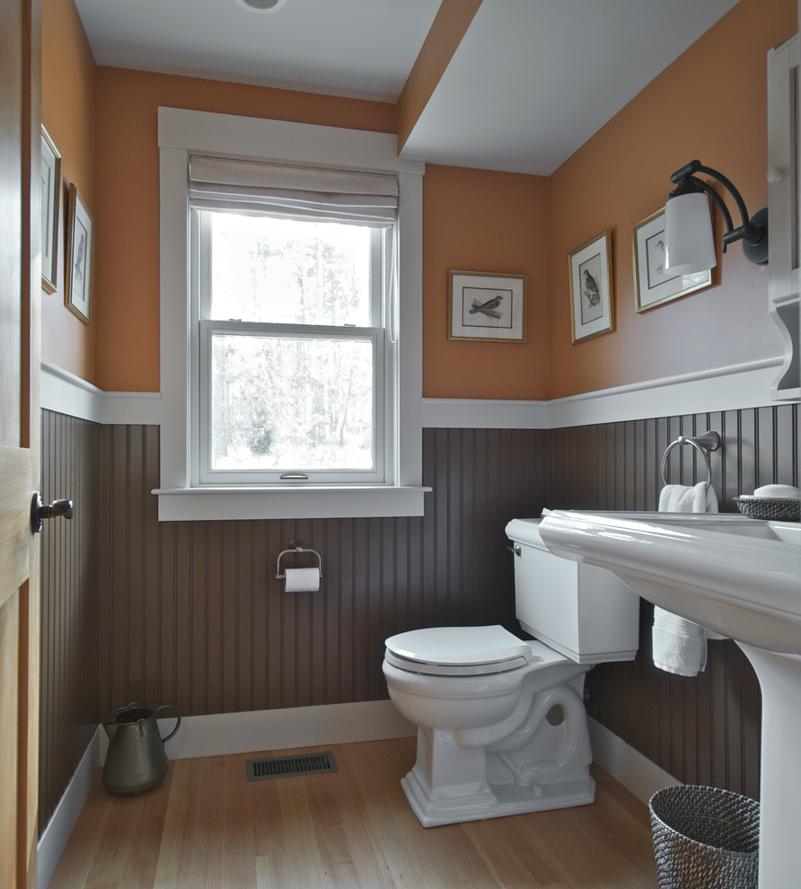 Klassisk inredning av ett litet badrum, med orange väggar, ljust trägolv och ett piedestal handfat