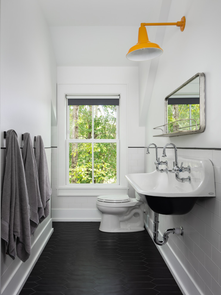 Lantlig inredning av ett stort badrum för barn, med en dusch i en alkov, en toalettstol med separat cisternkåpa, vit kakel, tunnelbanekakel, vita väggar, klinkergolv i keramik, ett avlångt handfat, svart golv och med dusch som är öppen