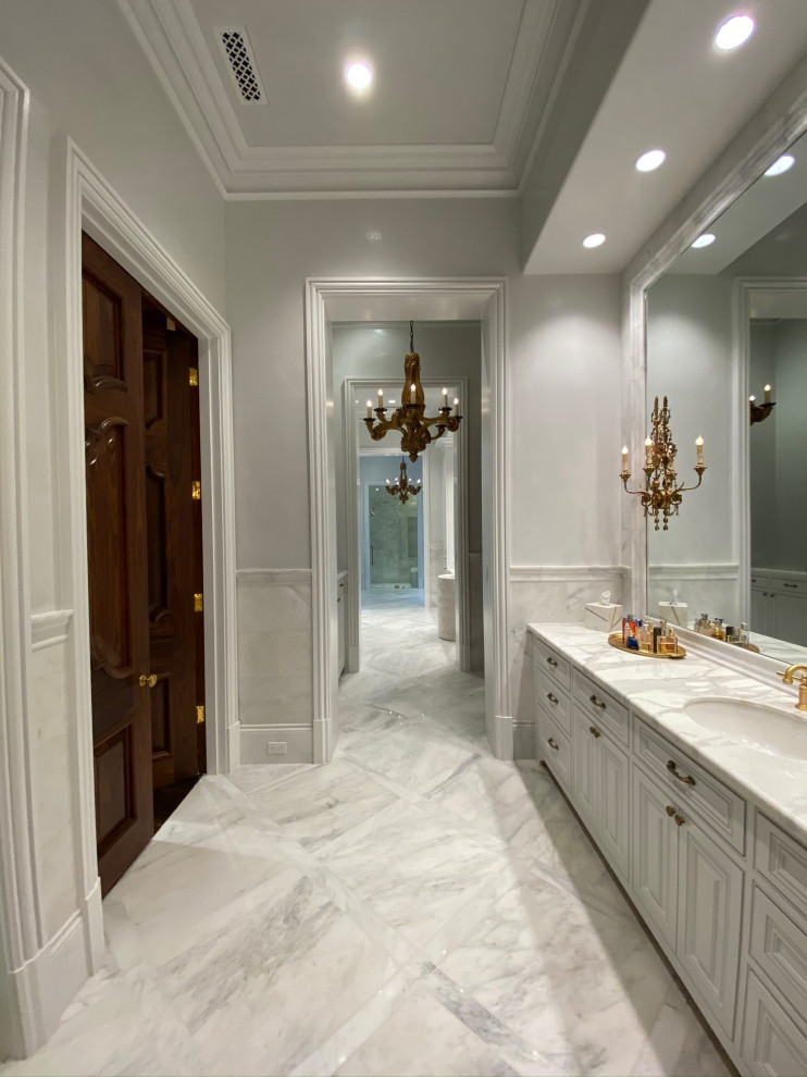 Modelo de cuarto de baño principal, doble y a medida extra grande con armarios con paneles con relieve, puertas de armario blancas y encimera de mármol