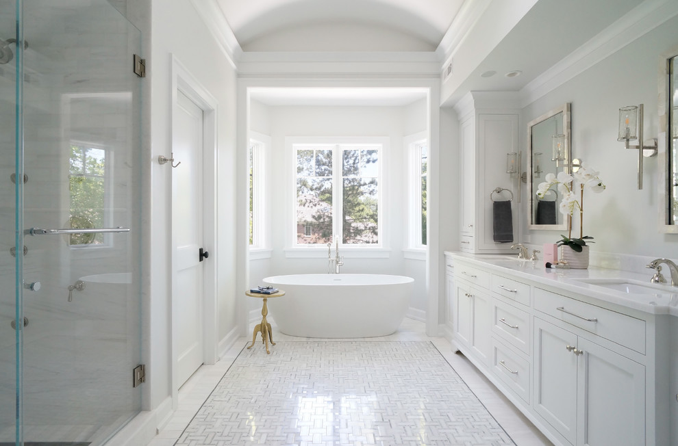 Идея дизайна: главная ванная комната в стиле неоклассика (современная классика) с фасадами с утопленной филенкой, белыми фасадами, отдельно стоящей ванной, угловым душем, белой плиткой, белыми стенами, полом из мозаичной плитки, врезной раковиной, белым полом, душем с распашными дверями и белой столешницей