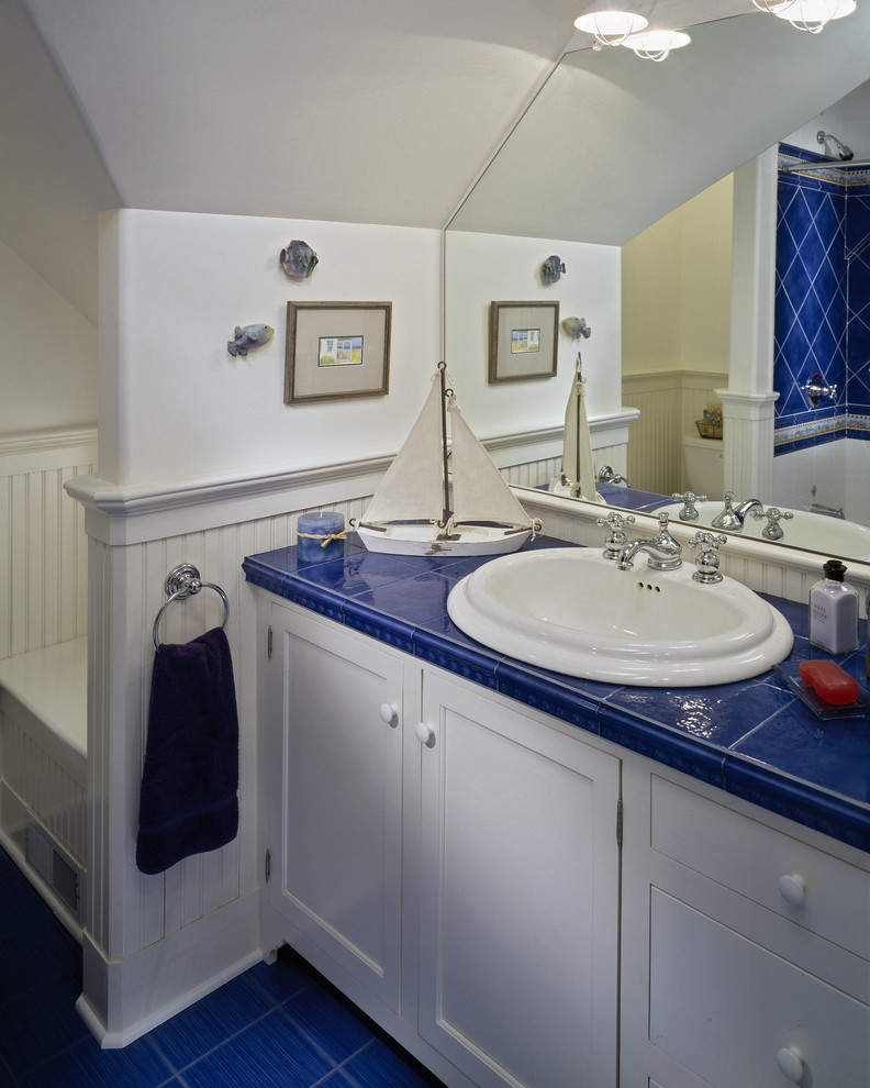 Maritimes Badezimmer mit Einbauwaschbecken, Schrankfronten mit vertiefter Füllung, weißen Schränken, Duschbadewanne, blauen Fliesen, gefliestem Waschtisch, blauem Boden und blauer Waschtischplatte in New York