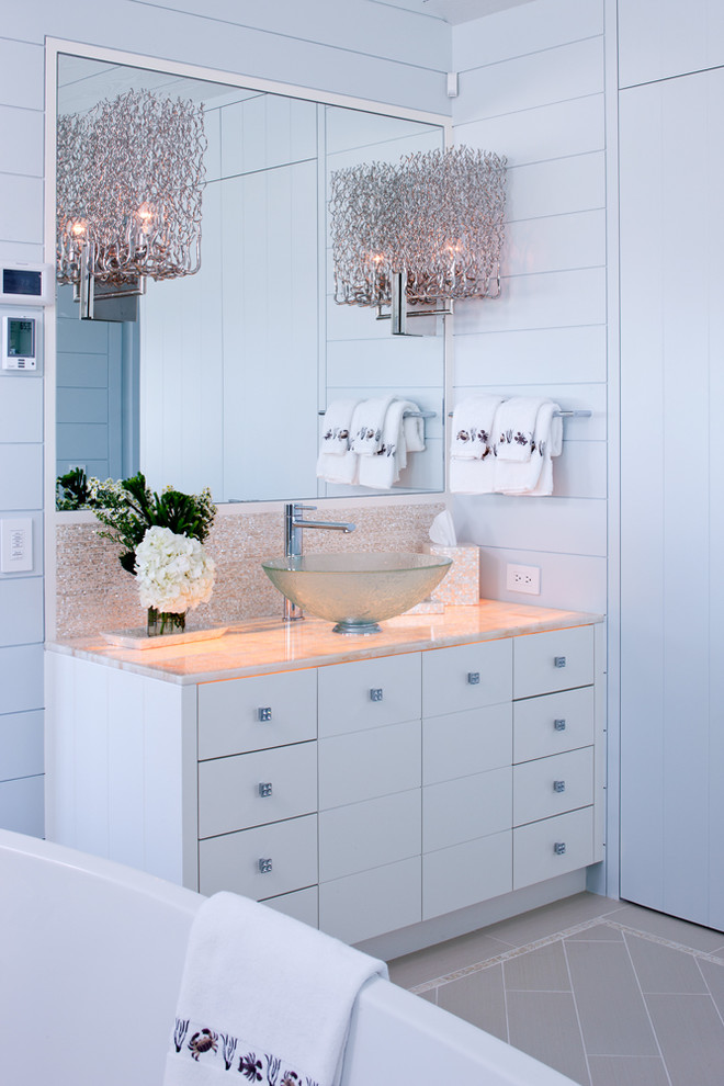 Maritim inredning av ett litet en-suite badrum, med ett fristående handfat, släta luckor, vita skåp, bänkskiva i onyx, ett fristående badkar, blå väggar och travertin golv
