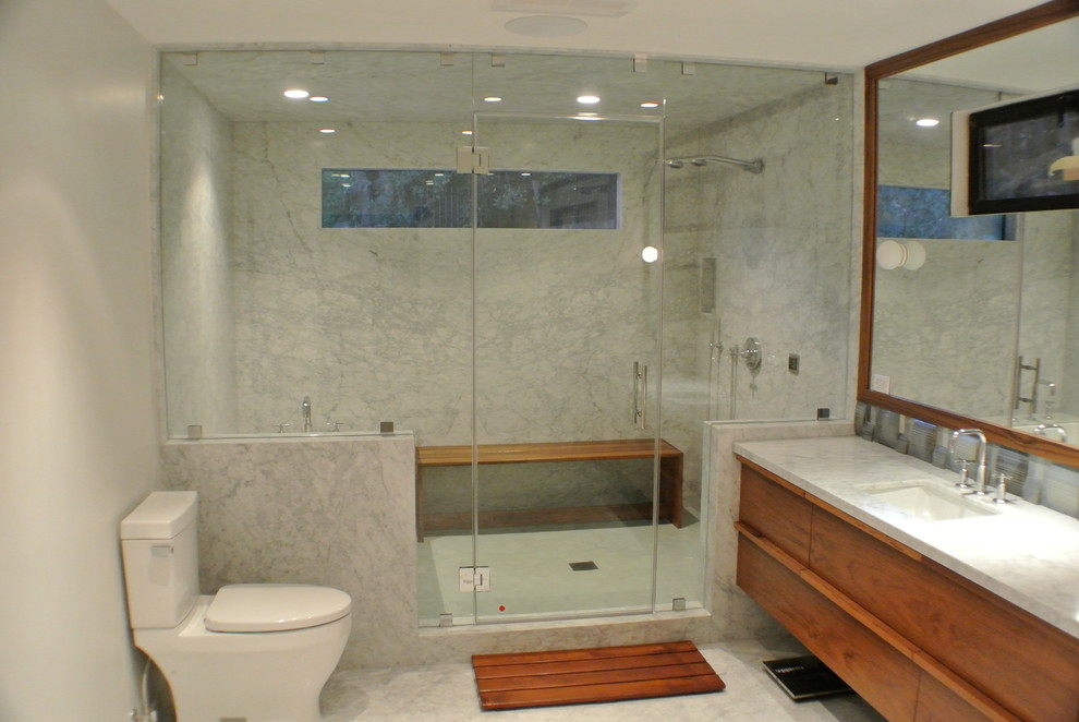 Réalisation d'une salle de bain design avec un lavabo encastré, une baignoire encastrée, un combiné douche/baignoire, WC séparés, un placard en trompe-l'oeil, des portes de placard marrons, un plan de toilette en marbre et un carrelage gris.