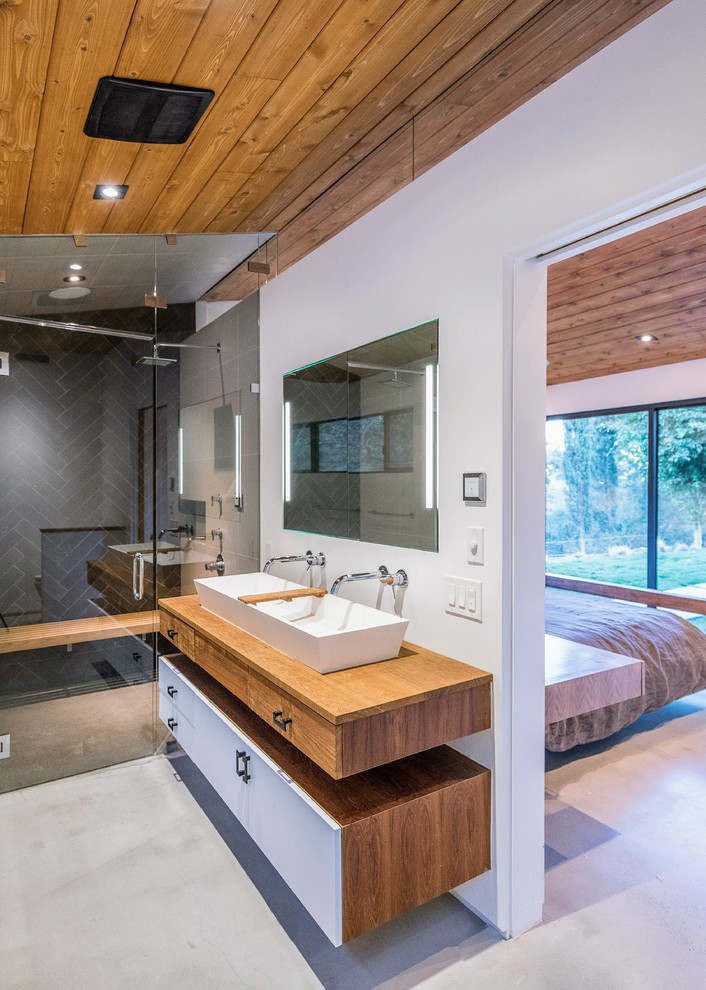 Example of a large trendy master black tile and cement tile concrete floor and gray floor alcove shower design in Los Angeles with flat-panel cabinets, white cabinets, white walls, a trough sink, wood countertops, a hinged shower door and brown countertops