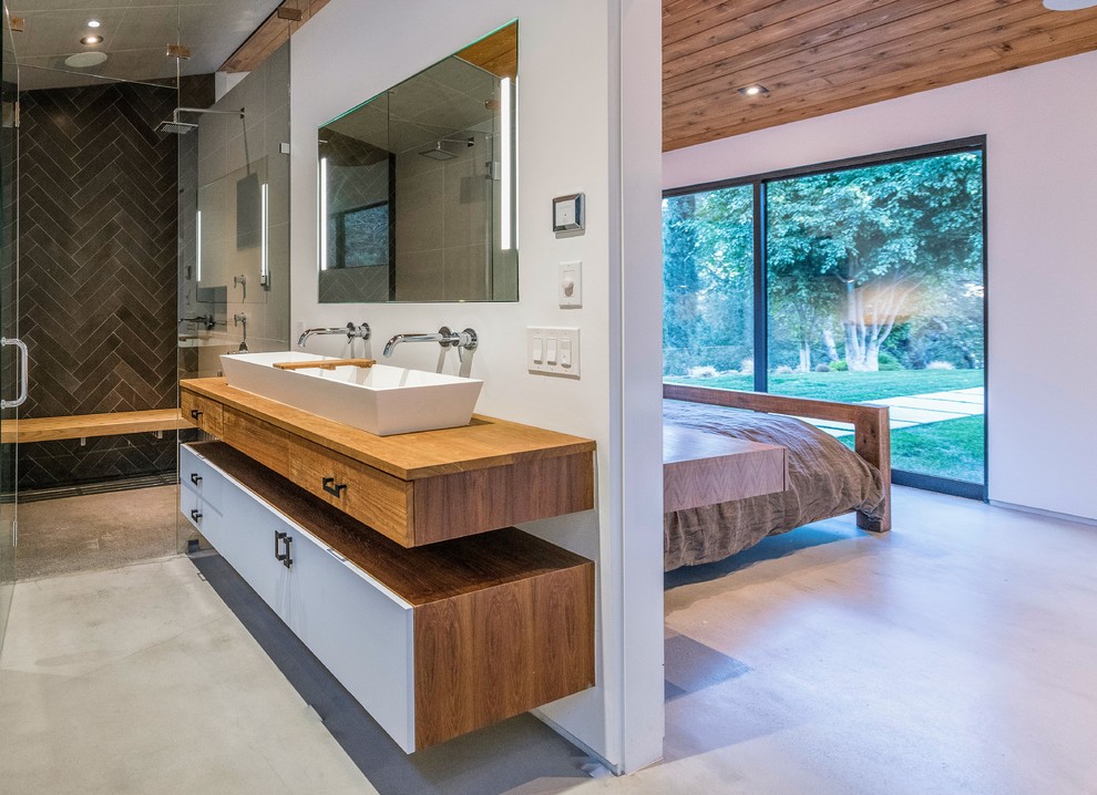 Contemporary ensuite bathroom in Los Angeles with flat-panel cabinets, white cabinets, a built-in shower, black tiles, grey tiles, white walls, concrete flooring, a trough sink, wooden worktops, grey floors, a hinged door and brown worktops.
