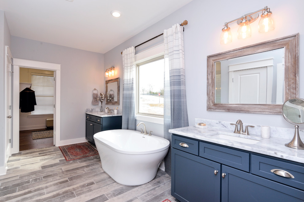 Cottage master blue tile brown floor freestanding bathtub photo in St Louis with shaker cabinets, blue cabinets, blue walls, an undermount sink, marble countertops and gray countertops