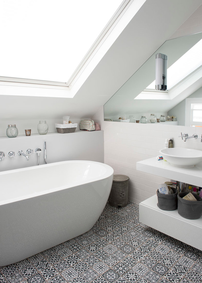 Стильный дизайн: ванная комната в современном стиле с плоскими фасадами, белыми фасадами, отдельно стоящей ванной, белой плиткой, плиткой кабанчик, белыми стенами, настольной раковиной и черным полом - последний тренд