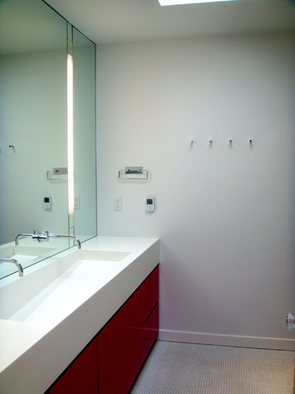 Cette photo montre une salle d'eau moderne de taille moyenne avec un placard à porte plane, des portes de placard rouges et un plan de toilette en surface solide.
