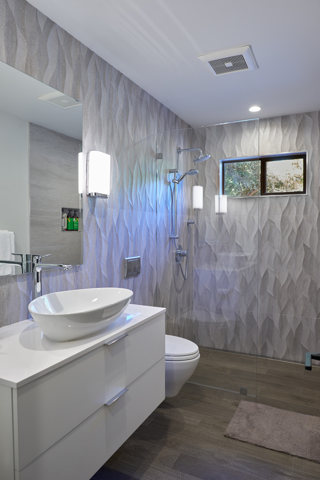 Medium sized contemporary ensuite bathroom in San Francisco with flat-panel cabinets, white cabinets, a built-in shower, a wall mounted toilet, grey tiles, ceramic tiles, grey walls, porcelain flooring, a vessel sink, engineered stone worktops, brown floors, an open shower and white worktops.