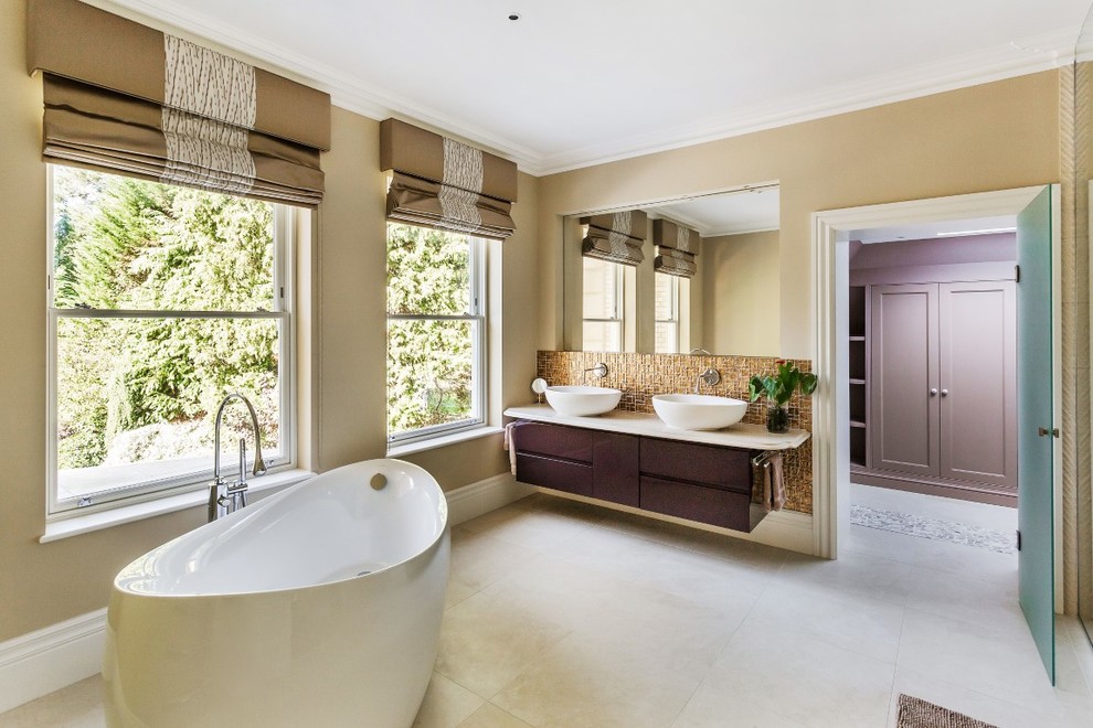 Design ideas for a traditional ensuite bathroom in Surrey with flat-panel cabinets, brown cabinets, a freestanding bath, beige tiles, beige walls, a vessel sink, beige floors and beige worktops.