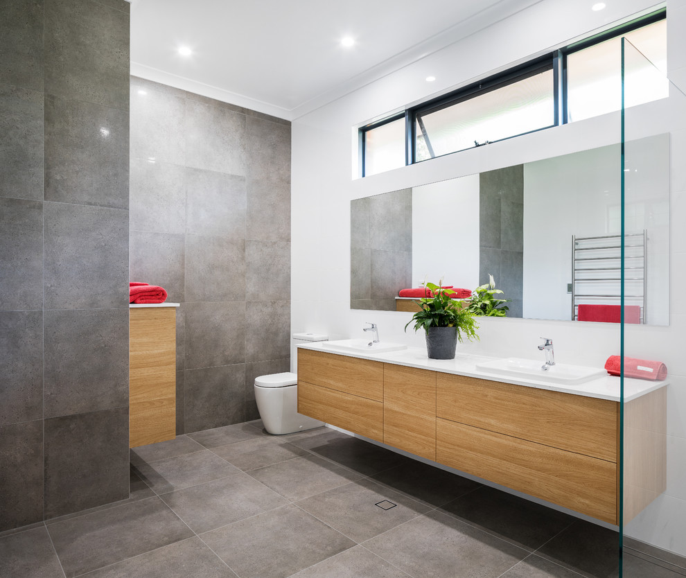 Modernes Badezimmer mit flächenbündigen Schrankfronten, hellbraunen Holzschränken, Quarzwerkstein-Waschtisch, Toilette mit Aufsatzspülkasten, grauen Fliesen, weißer Wandfarbe, Aufsatzwaschbecken und weißer Waschtischplatte in Perth