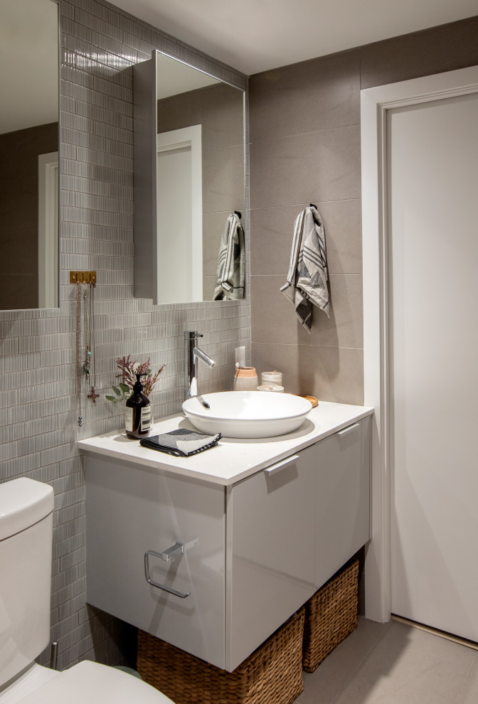 Esempio di una stanza da bagno design con ante lisce, ante bianche, WC a due pezzi, piastrelle grigie, lavabo a bacinella, pavimento grigio e top bianco