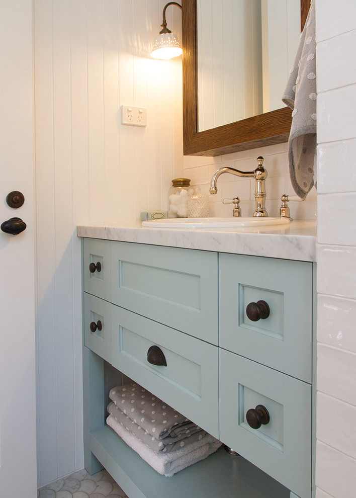 Bild på ett mellanstort lantligt badrum för barn, med luckor med infälld panel, en öppen dusch, vit kakel, keramikplattor, vita väggar, marmorbänkskiva, en toalettstol med separat cisternkåpa, marmorgolv, ett undermonterad handfat och turkosa skåp