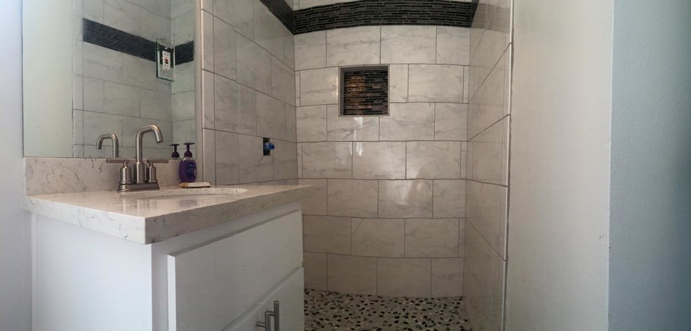 Réalisation d'une douche en alcôve principale tradition de taille moyenne avec un placard à porte plane, des portes de placard blanches, une plaque de galets, un mur blanc, un lavabo encastré et un plan de toilette en quartz modifié.