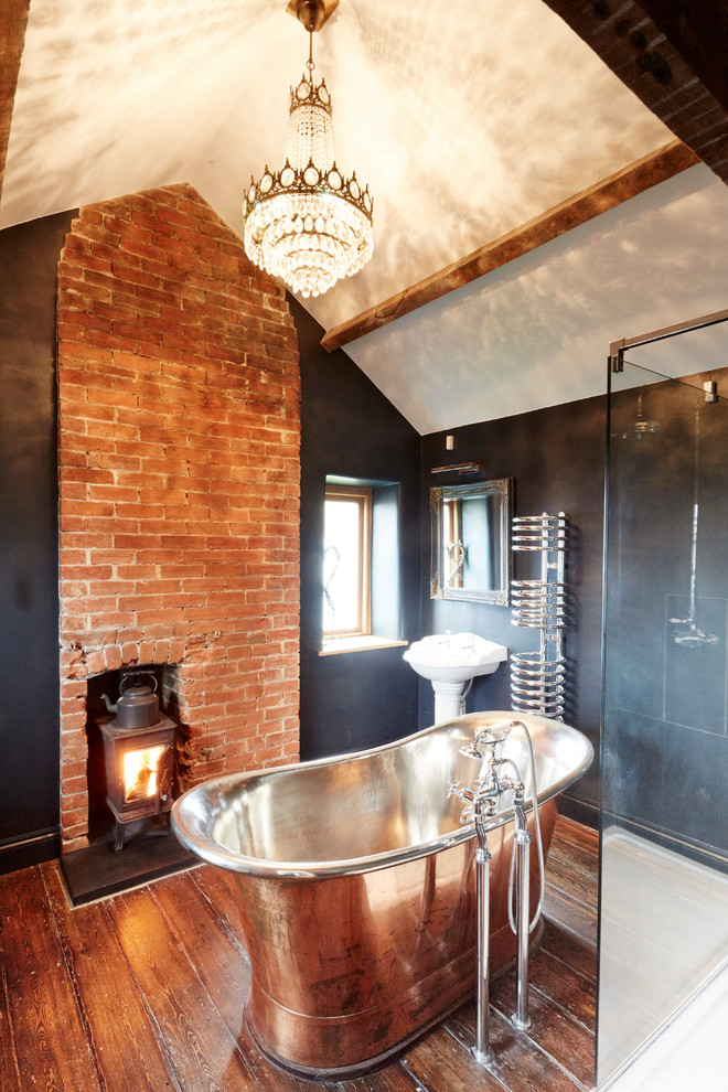 Mid-sized cottage master medium tone wood floor freestanding bathtub photo in Wiltshire with a pedestal sink, a wall-mount toilet and black walls