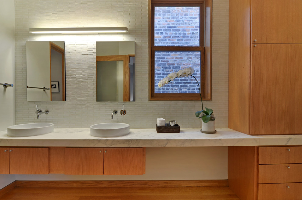Стильный дизайн: главная ванная комната в современном стиле с плоскими фасадами, фасадами цвета дерева среднего тона, мраморной столешницей, белой плиткой, настольной раковиной, каменной плиткой, белыми стенами и паркетным полом среднего тона - последний тренд