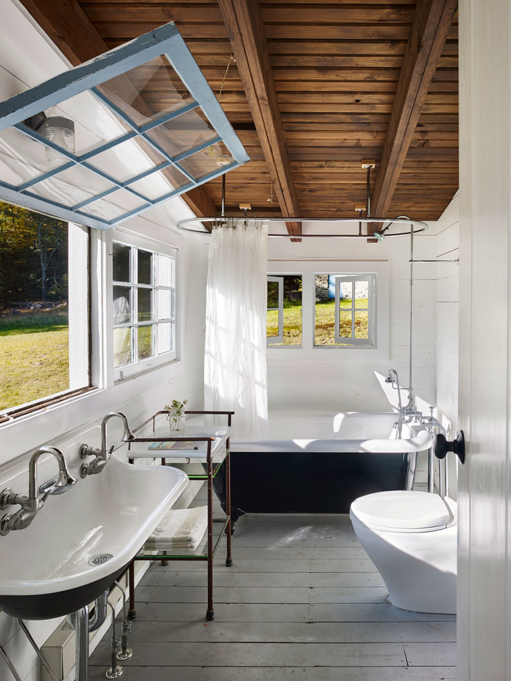 Diseño de cuarto de baño principal campestre con bañera con patas, combinación de ducha y bañera, paredes blancas, suelo de madera pintada, lavabo de seno grande, ducha con cortina y ventanas