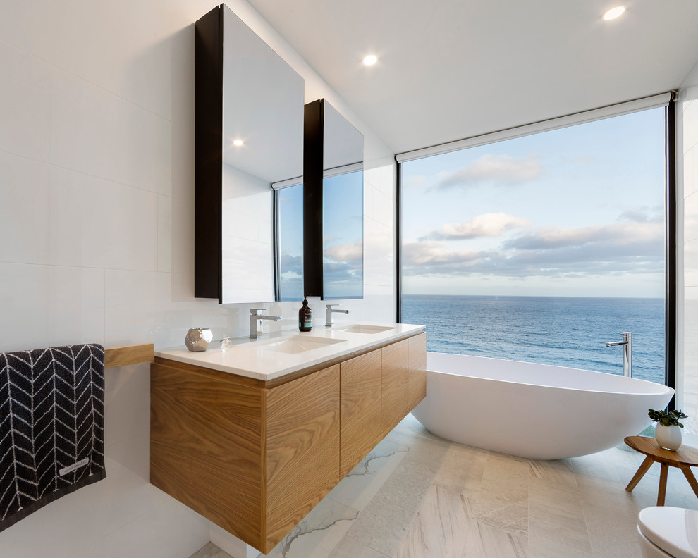 Пример оригинального дизайна: ванная комната в современном стиле с врезной раковиной, плоскими фасадами, фасадами цвета дерева среднего тона, отдельно стоящей ванной и белыми стенами